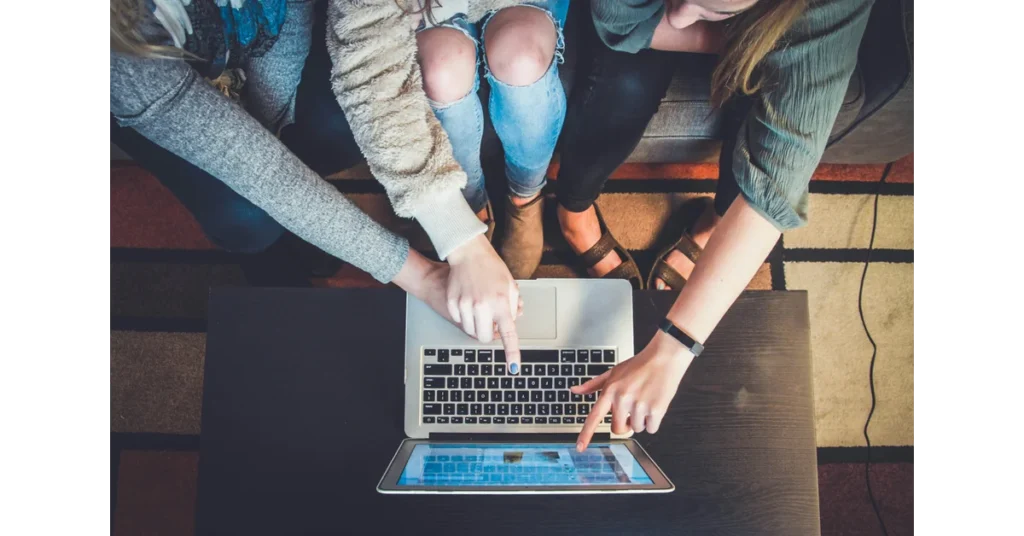 A group of people looking to a computer and pointing at it. 